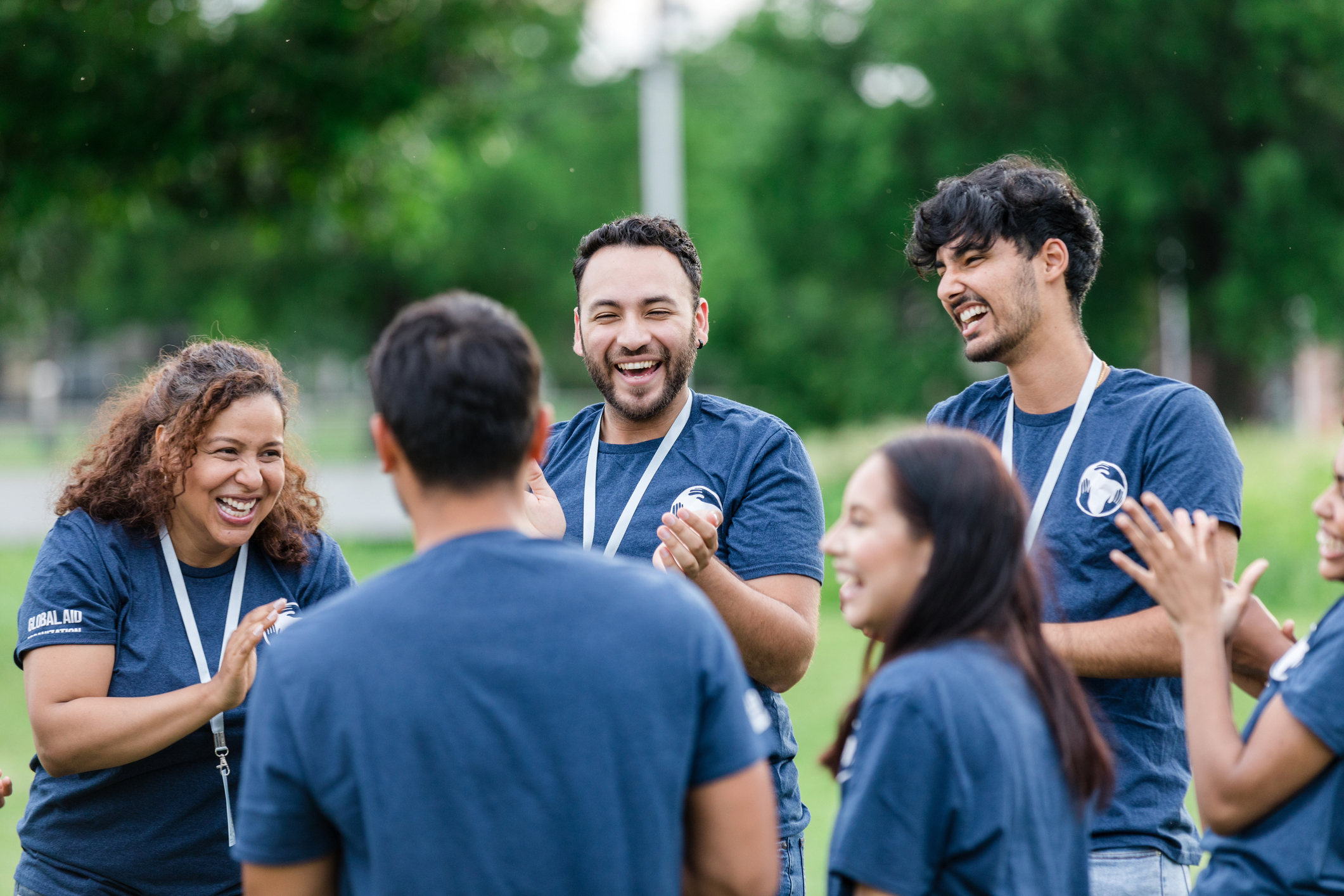A group of volunteers in matching t-shirts laughing and high-fiving outdoors
